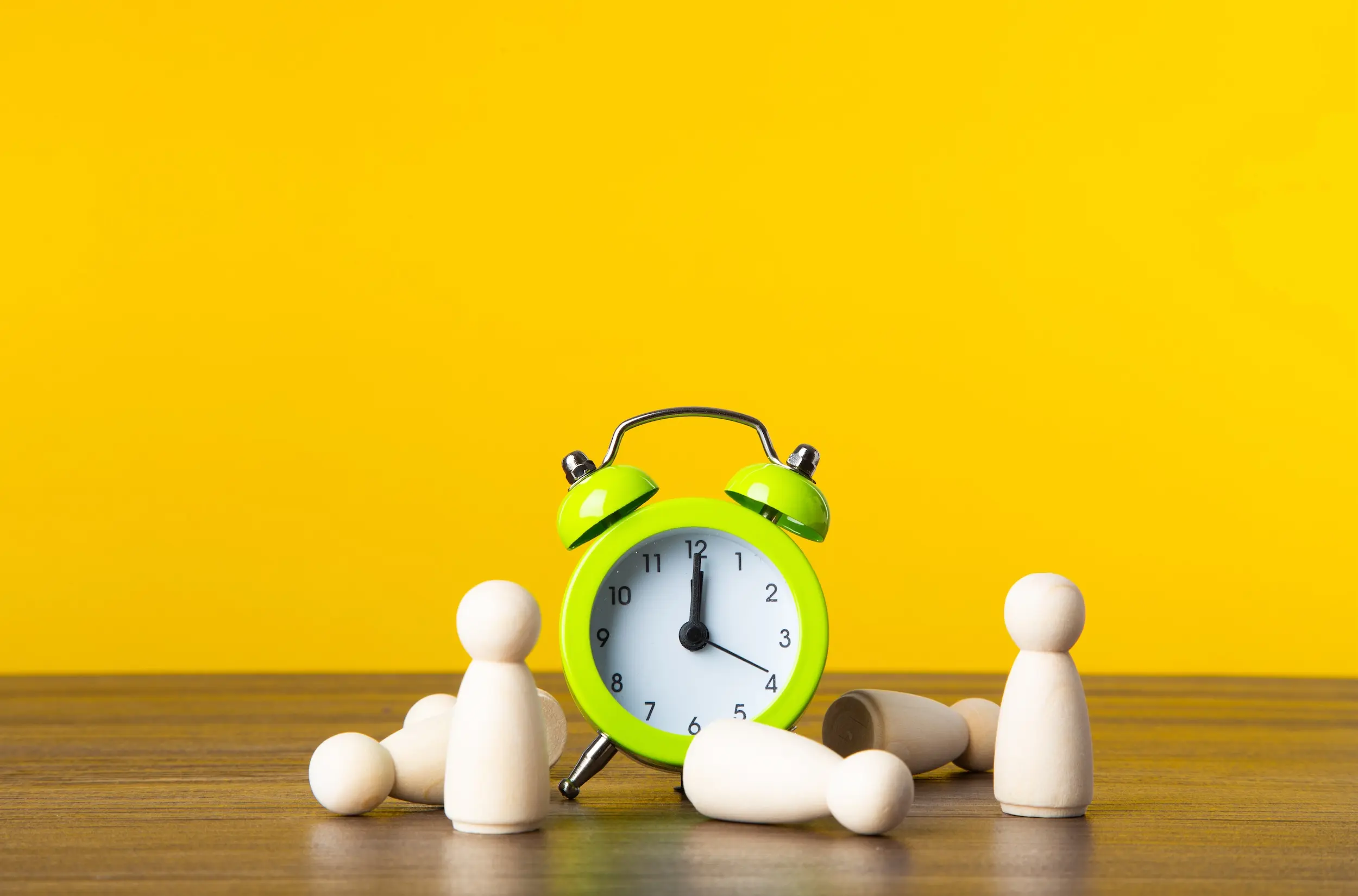 A clock and wooden pegs on a table with a yellow background.