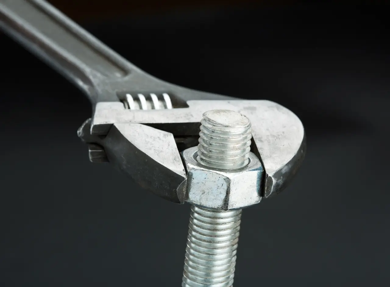 A silver wrench tightening a nut along the length of a sliver screw 