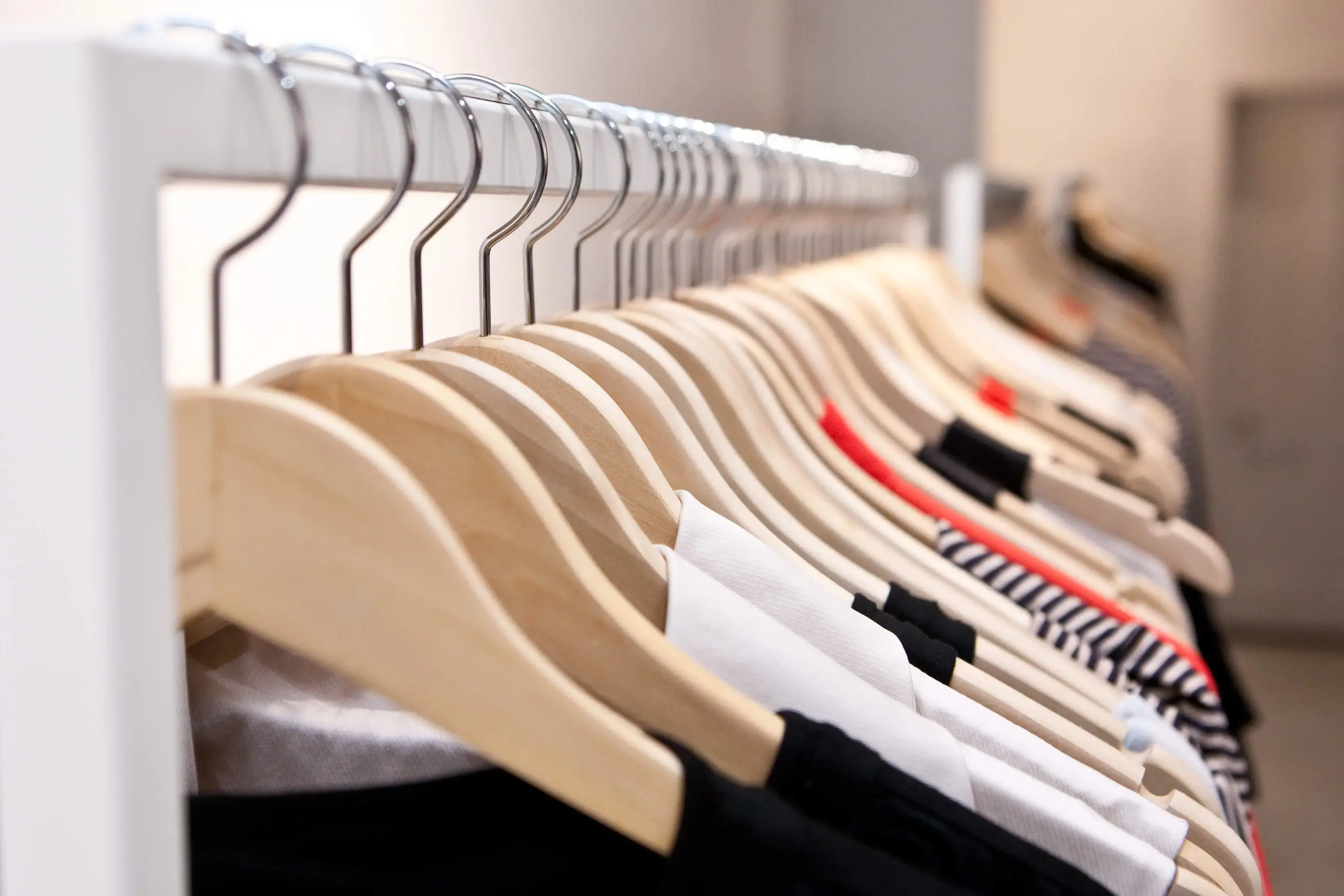 A diagonal view of a rack of clothes, with wood hangars and various shirts hanging from the rack. 