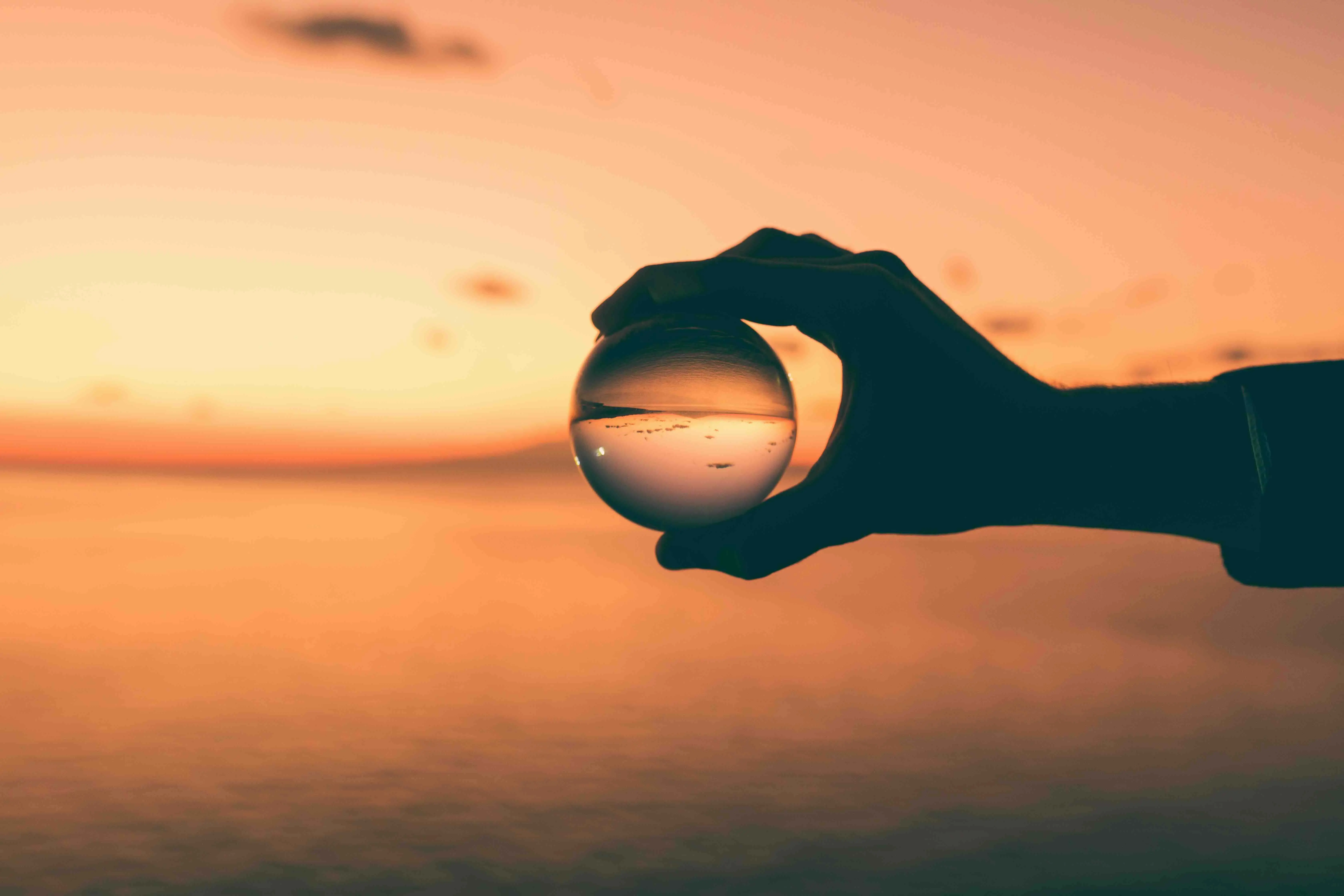 A hand holding a glass ball, magnifying a portion of the horizon in the distance