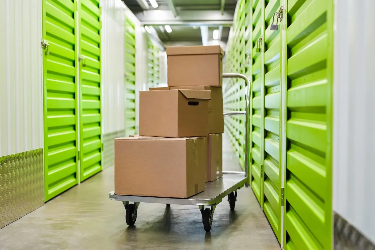 A cart with cardboard boxes on it in front of a series of bright green doors to storage units