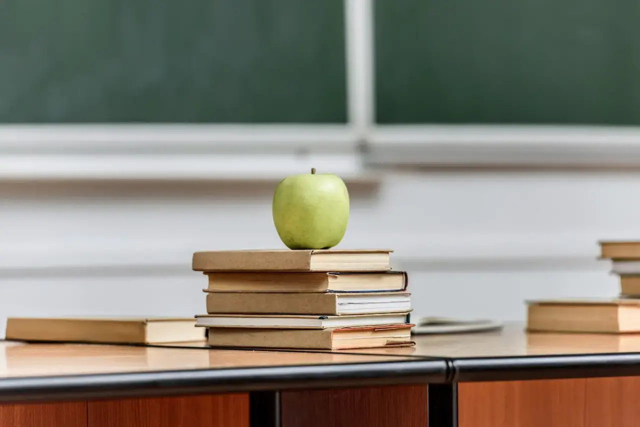 A green apple sitting on top of a stack of books with a blackboard in the background