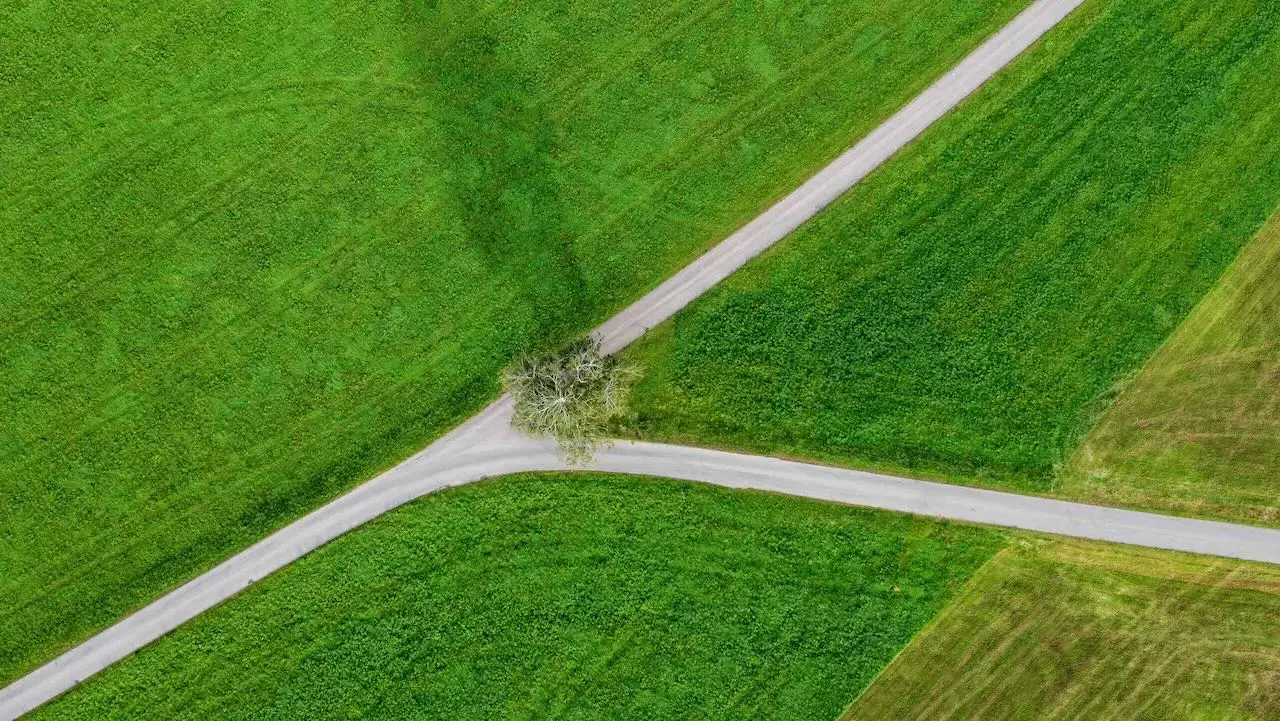 An overhead shot of a road that splits at a fork and continue through a green field
