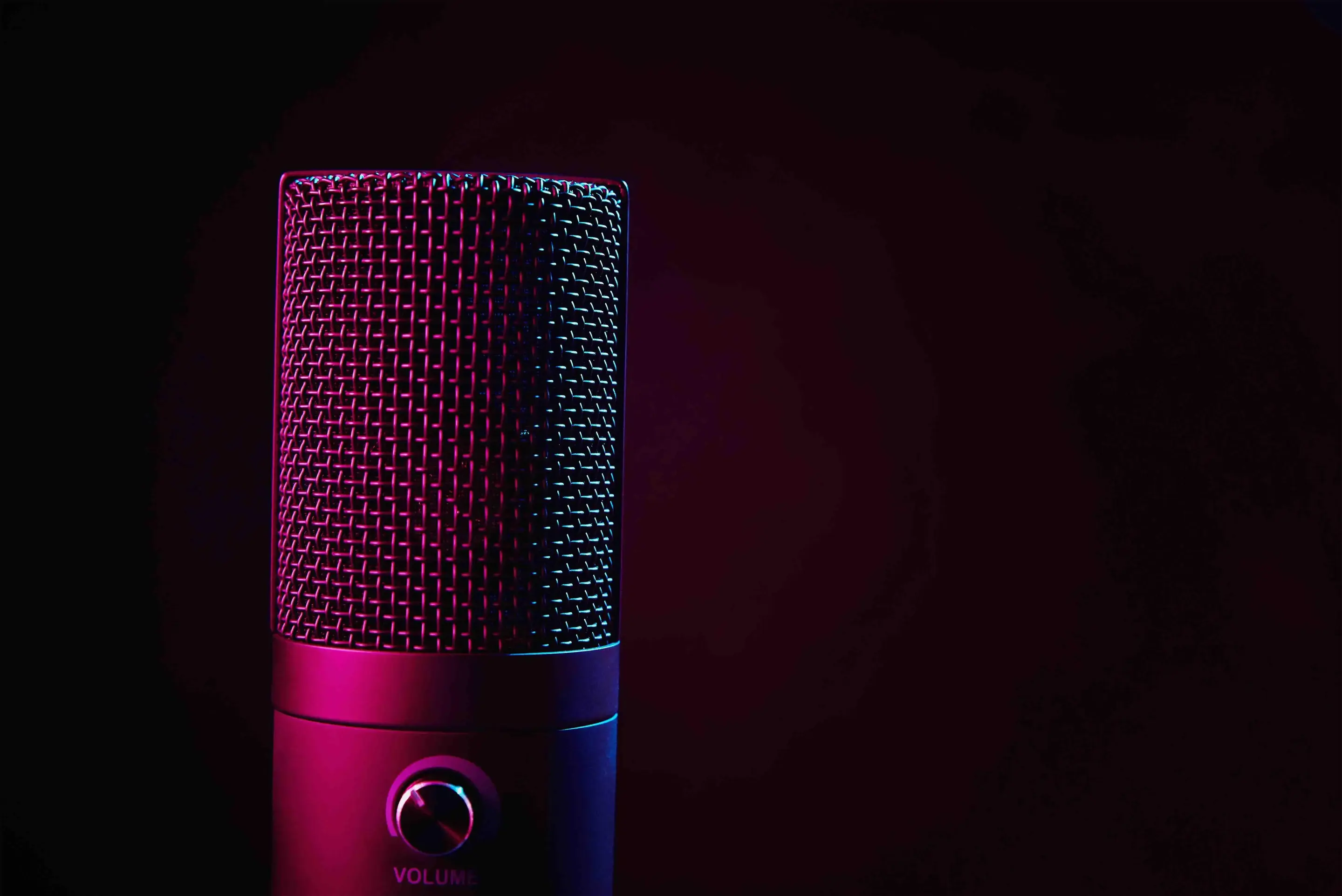 A studio microphone against a black background, lit with pink light in the foreground