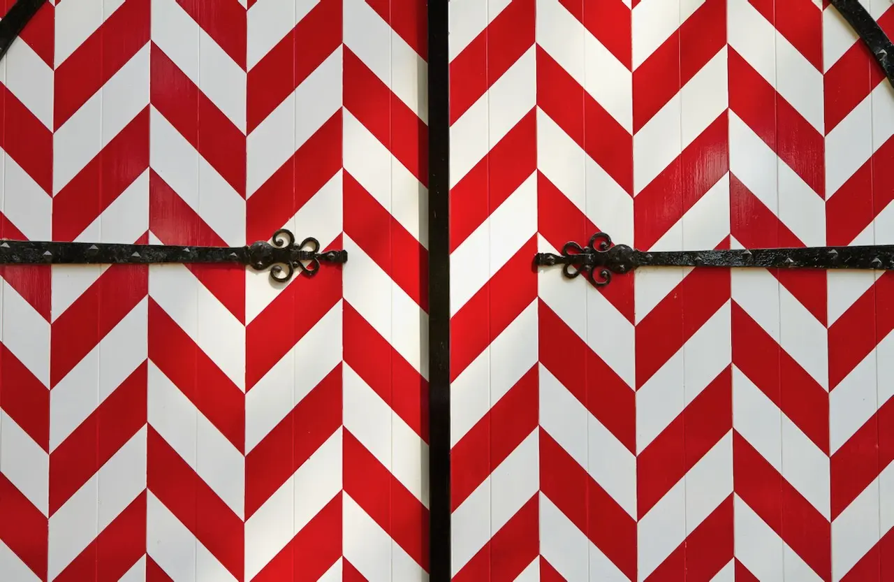 Two doors with a red and white chevron pattern and a decorative iron bar across the center of each door