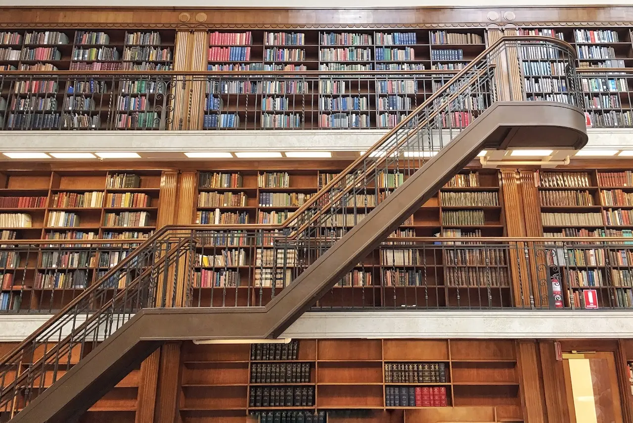 A staircase leading up past bookshelves lining the walls of multiple floors 