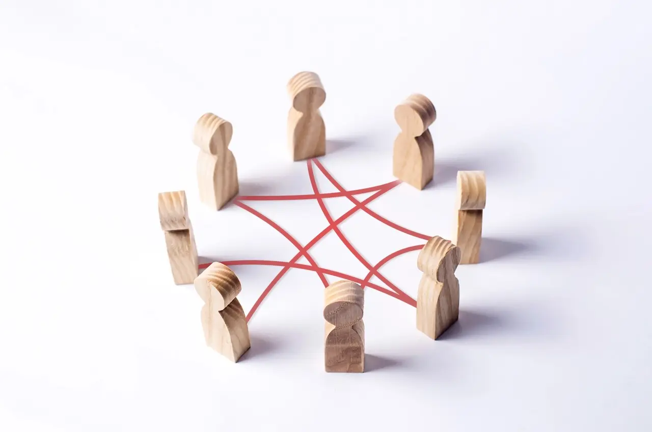 Small, person-shaped wood figures in a circle, with red lines connecting some figures to each other across the circle