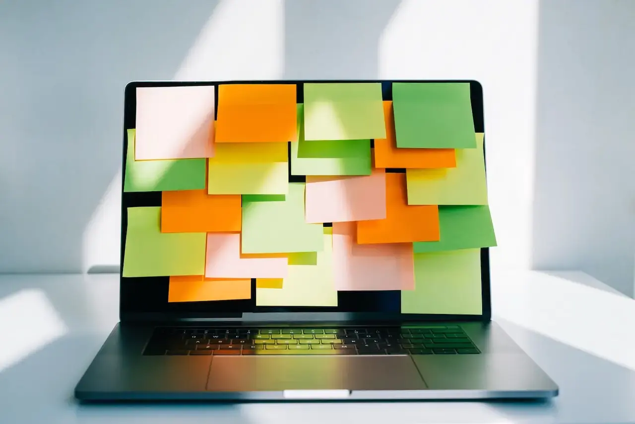 A laptop with the screen covered in multi-colored sticky notes 
