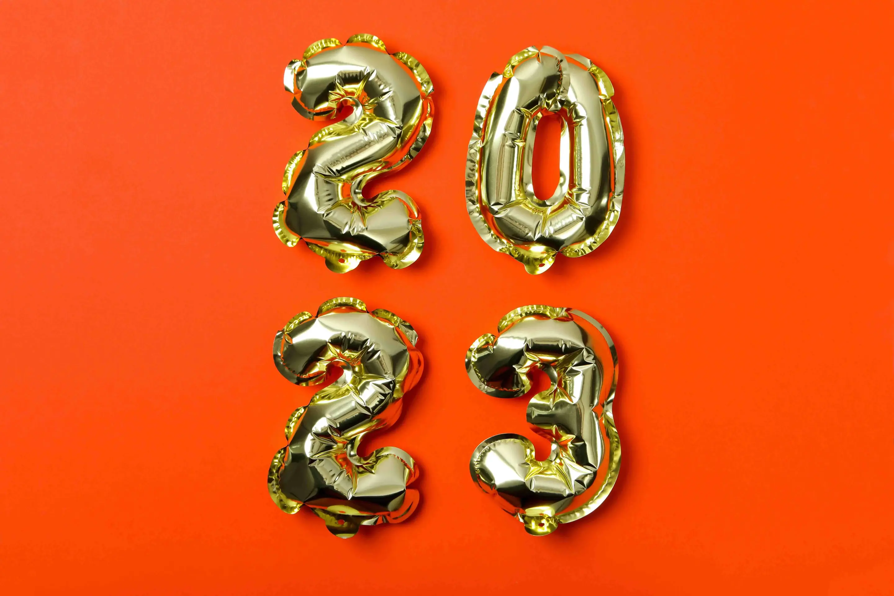 Metallic gold balloons in the form of the number 2023 against a red background