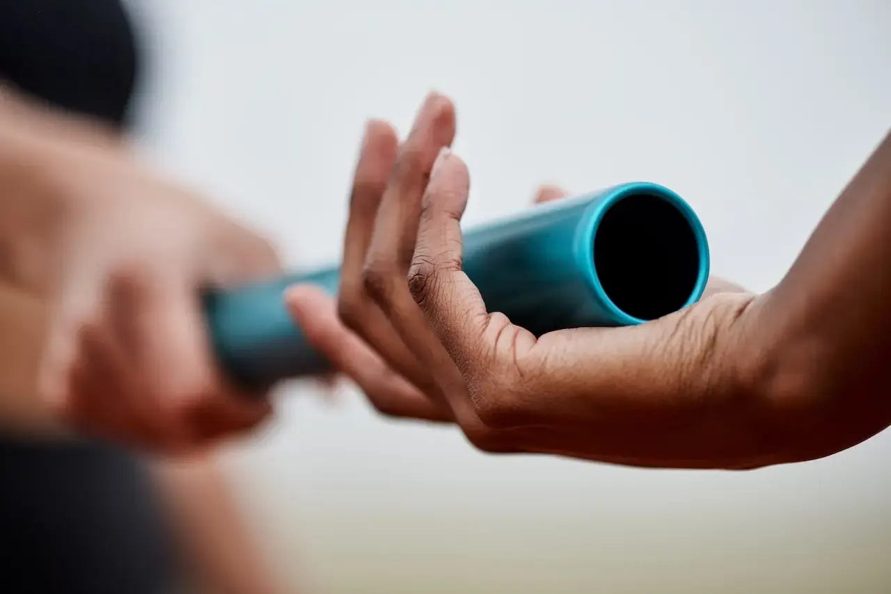 A blue relay baton being handed off from one person's hand to another person's hand