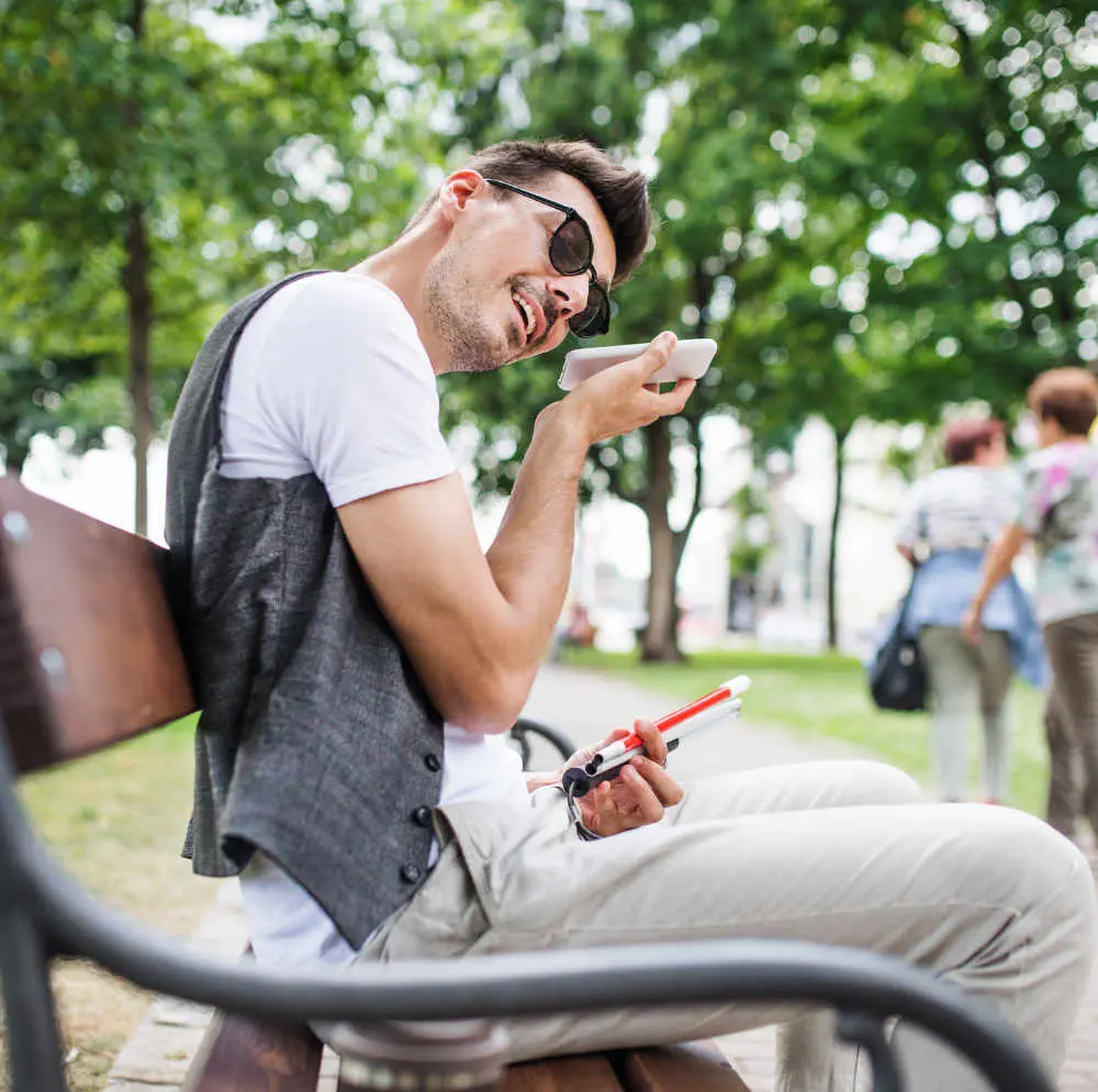 Visually impaired man sitting on bench using phone