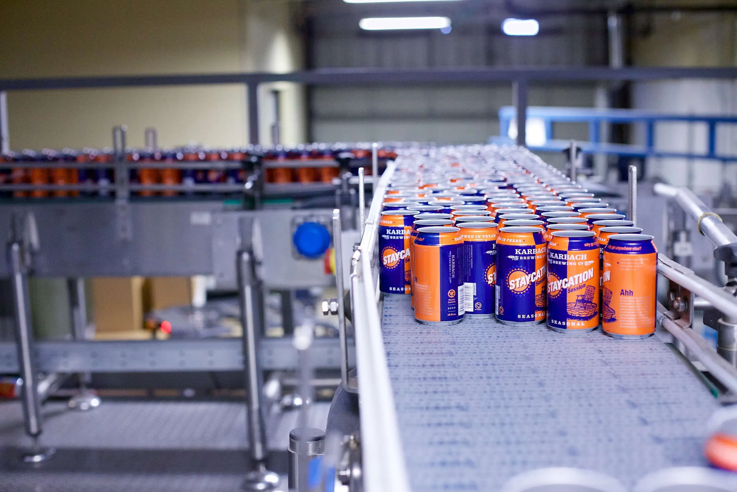 Orange and blue beer cans coming off a conveyor belt to be filled.