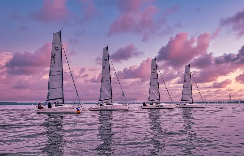 Four sailboats spread horizontally across the frame against a sunset