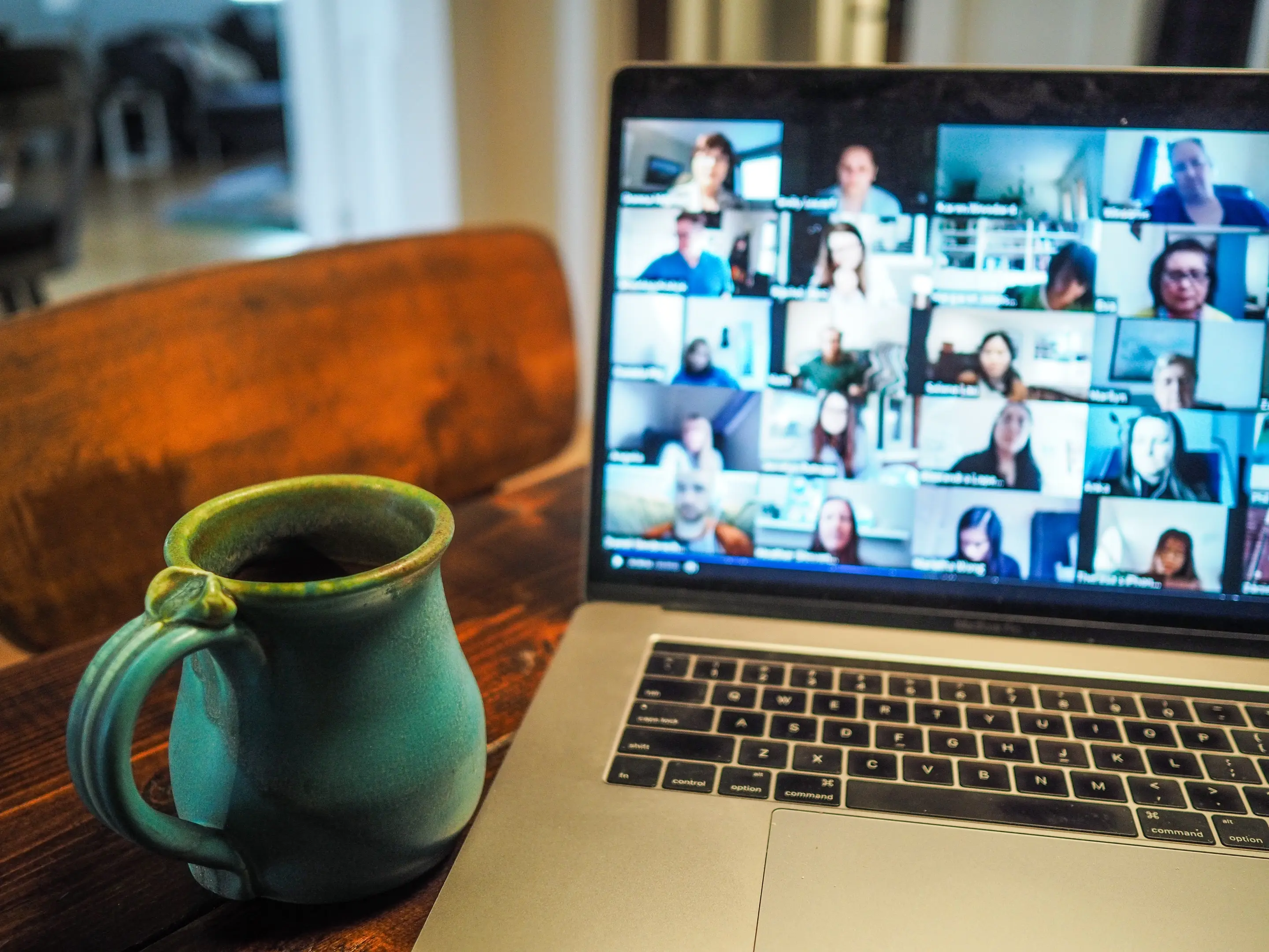 A mug next to an open laptop showing participants of a video meeting
