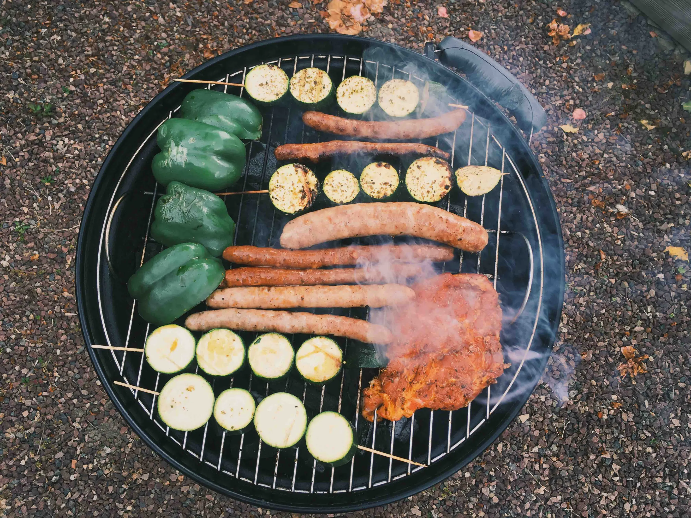 An overhead shot of sausages, zucchini, bell peppers, and chicken on a round grill.