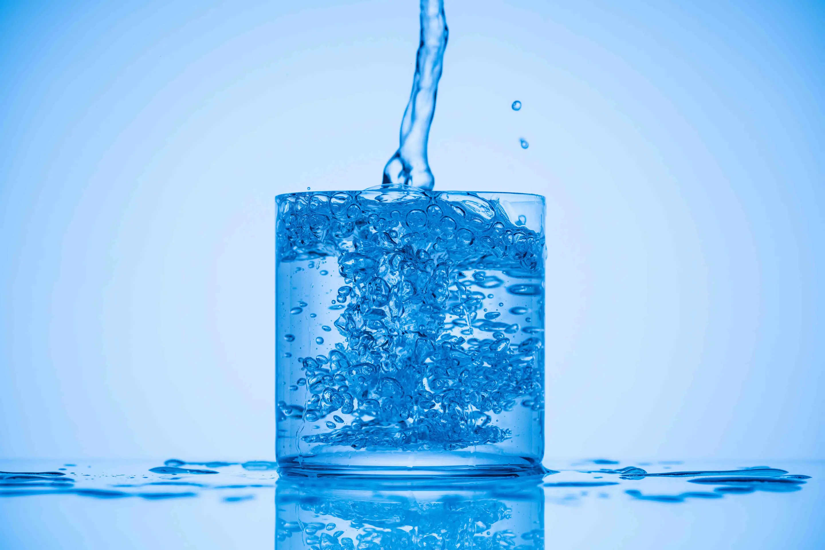 Water pouring into a full cup against a blue background