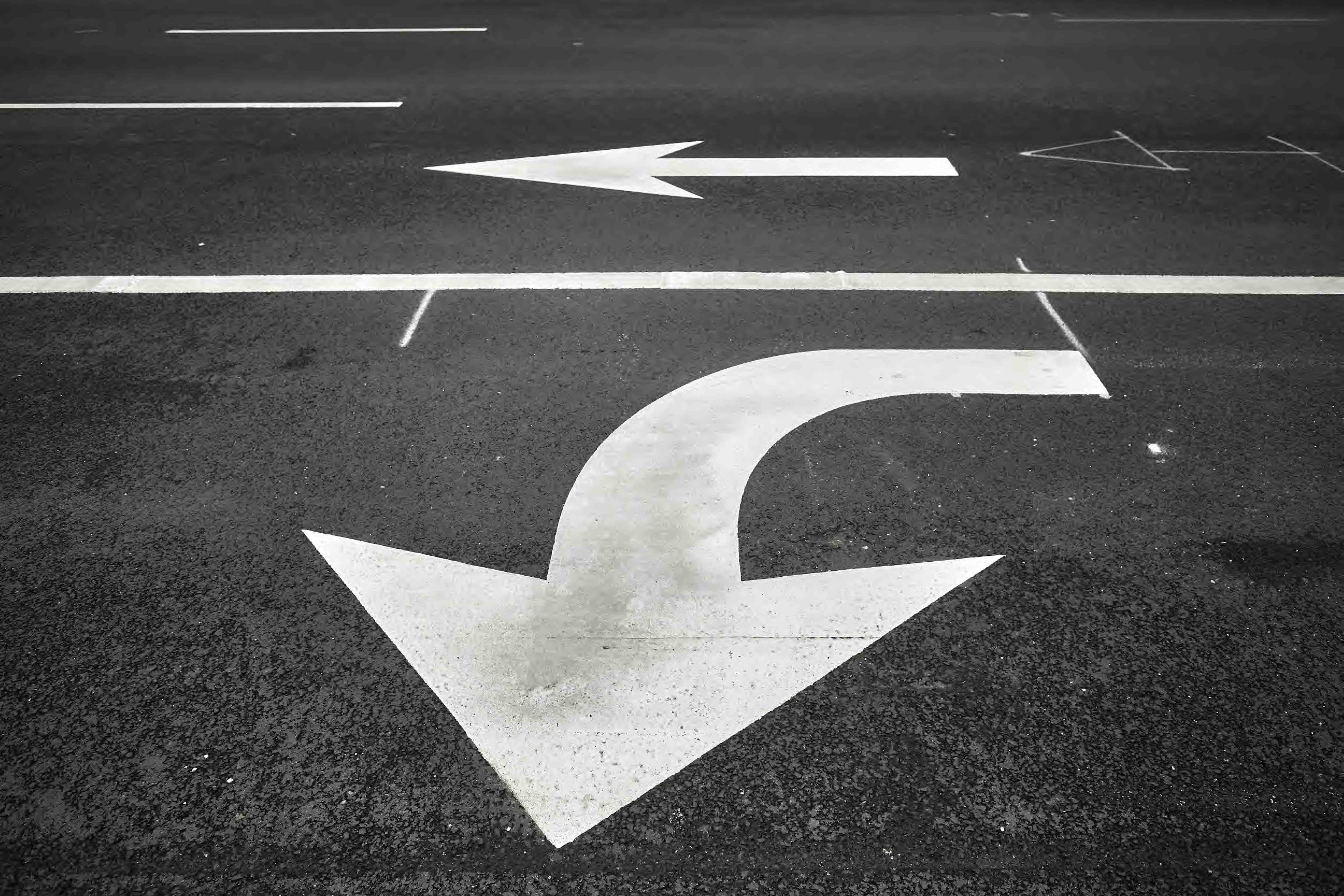 A turn arrow painted in white on black asphalt next to a separate straight arrow