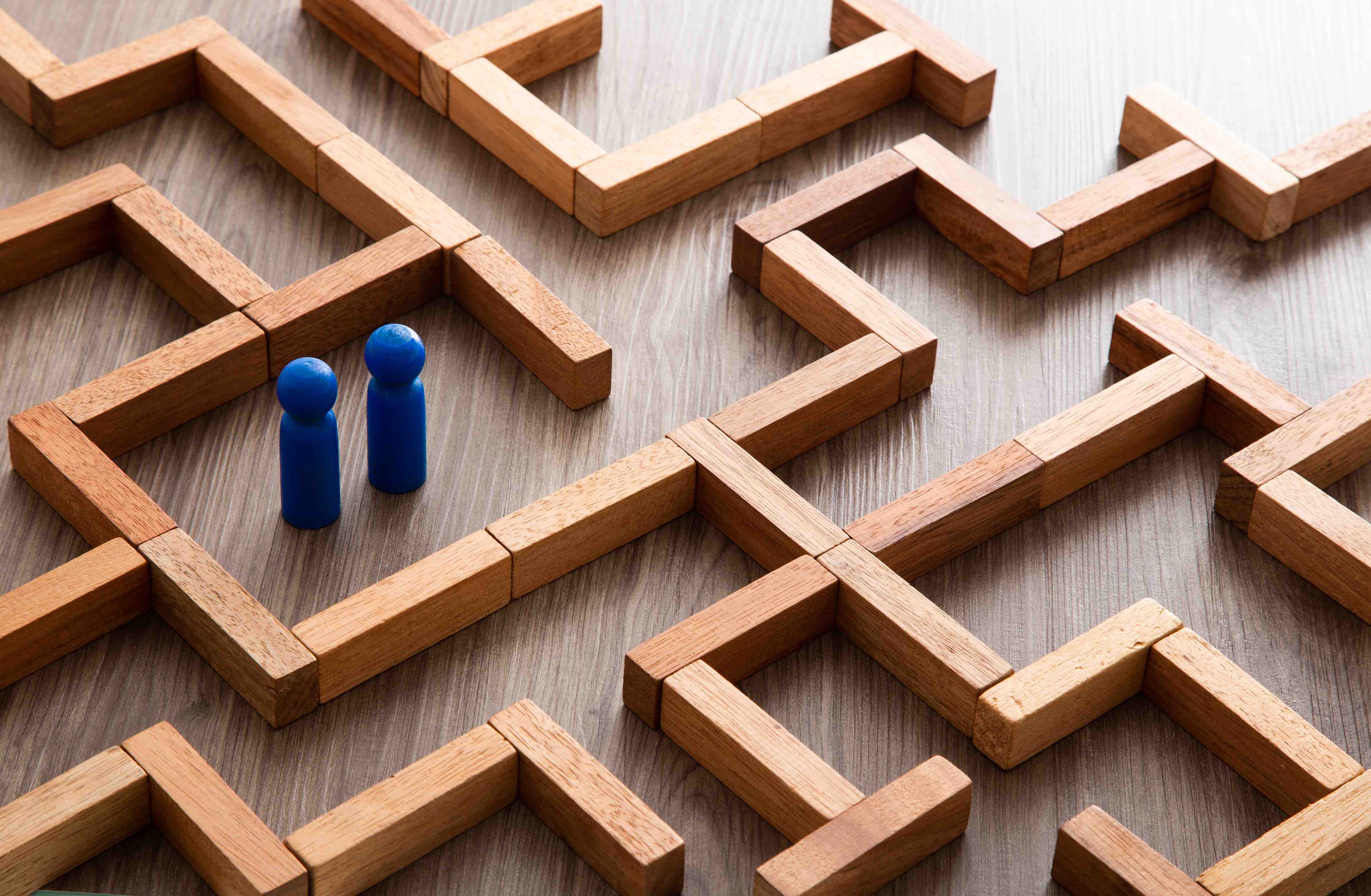 Two blue game figures sanding at the center of a maze made of wooden blocks 