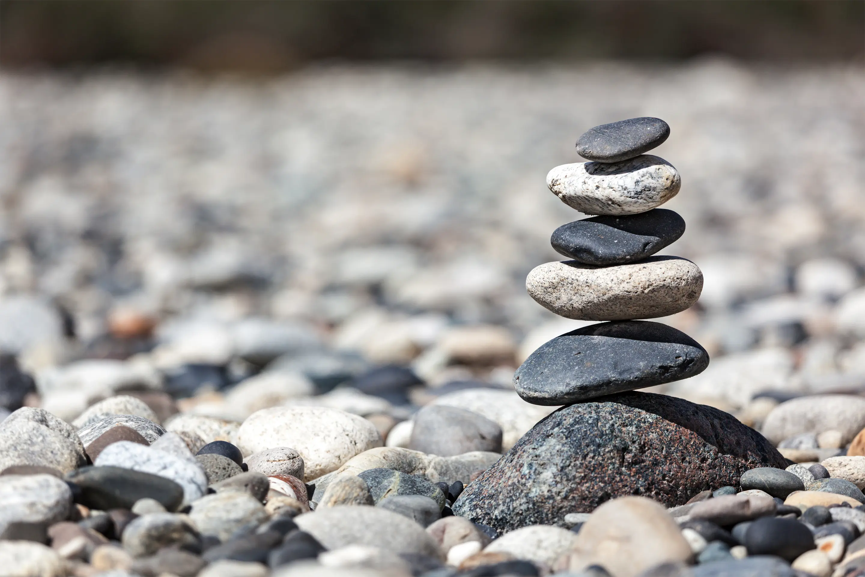 A stack of small stones balanced one on top of the other, with a stony beach in the background.