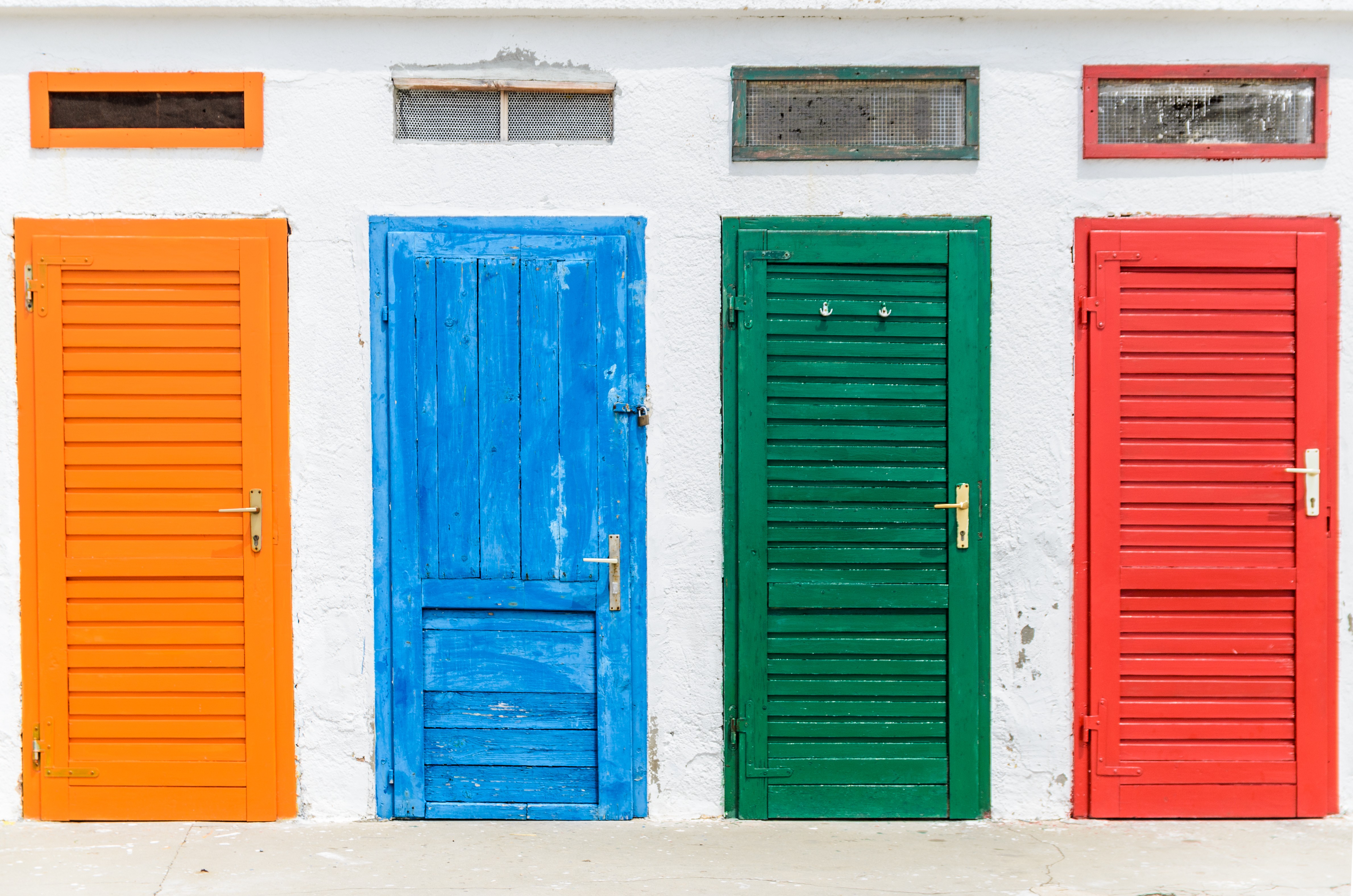 Four colorful wooden doors in a row. From left to right: orange, blue, green, red.