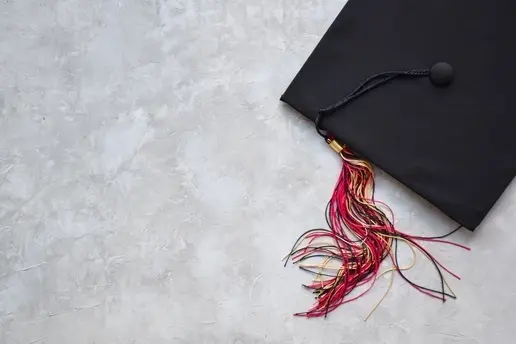 A black graduation cap and red tassle against a yellow background